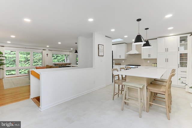 kitchen with wall chimney exhaust hood, white cabinets, light countertops, a kitchen breakfast bar, and backsplash