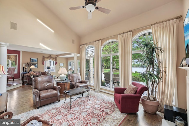 living area with wood finished floors, a ceiling fan, plenty of natural light, high vaulted ceiling, and decorative columns