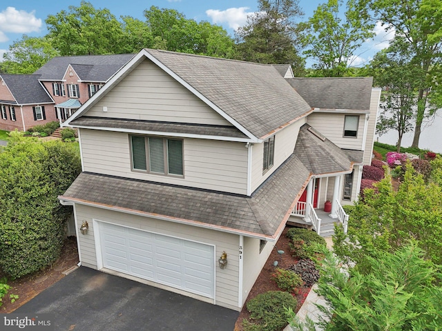 traditional-style home featuring an attached garage, asphalt driveway, and roof with shingles