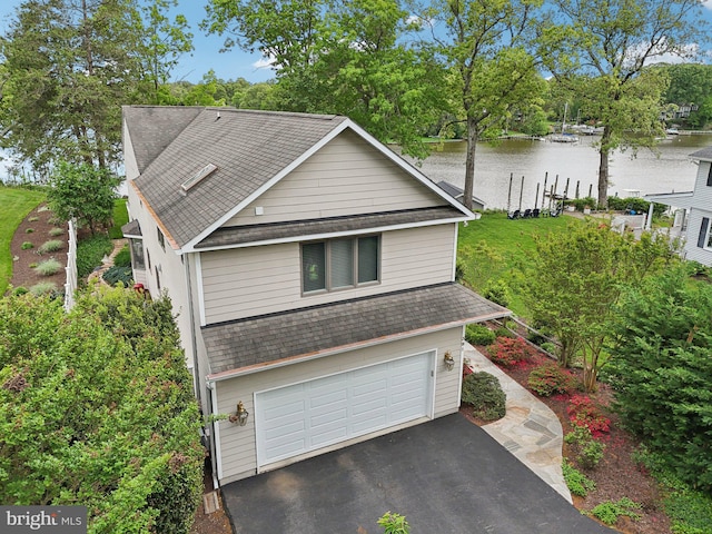 view of front facade featuring a shingled roof, an attached garage, a water view, and driveway