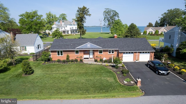 view of front facade featuring driveway, brick siding, an attached garage, a water view, and a front lawn