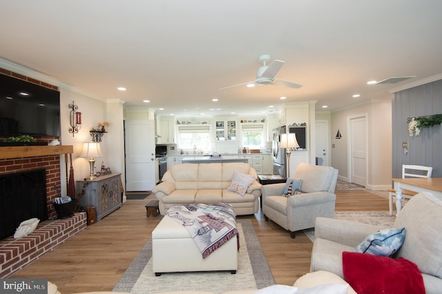 living room featuring recessed lighting, a fireplace, crown molding, light wood finished floors, and a ceiling fan
