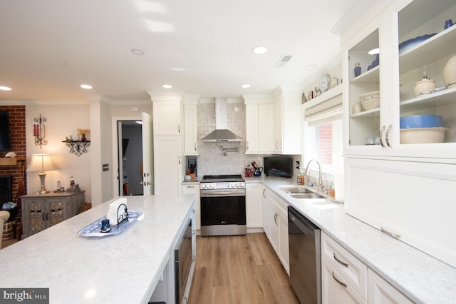 kitchen featuring a sink, wall chimney range hood, ornamental molding, white cabinetry, and appliances with stainless steel finishes