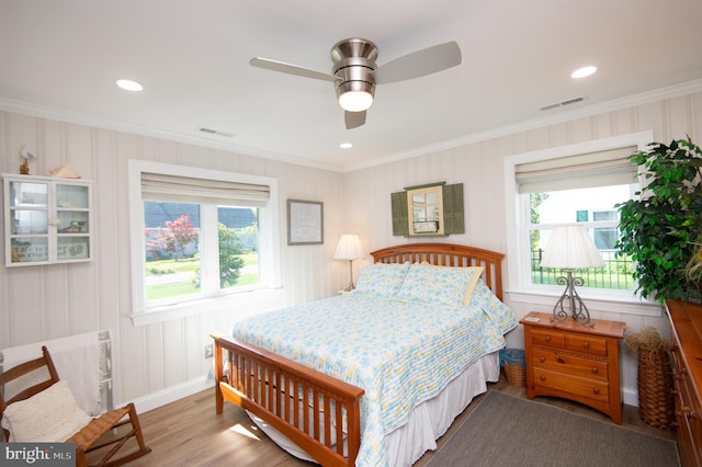 bedroom with a ceiling fan, crown molding, visible vents, and wood finished floors