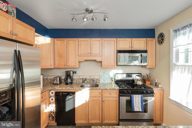 kitchen with appliances with stainless steel finishes, a sink, light brown cabinets, light stone countertops, and decorative backsplash