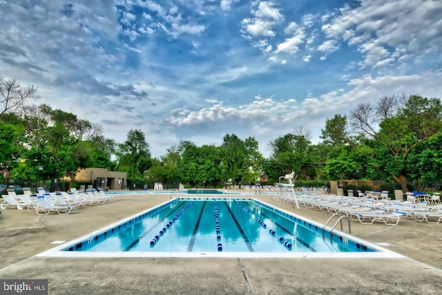 community pool with a patio, view of scattered trees, and fence