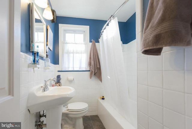 bathroom featuring tile walls, tile patterned floors, toilet, shower / bath combo with shower curtain, and wainscoting