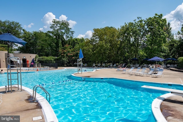 community pool with fence, a patio, view of scattered trees, and a diving board