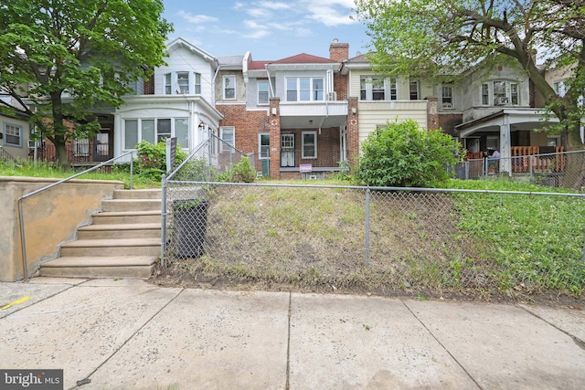 view of property featuring a chimney, brick siding, a fenced front yard, central air condition unit, and stairway