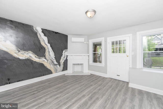 unfurnished living room featuring wood finished floors, baseboards, a wall mounted AC, and a fireplace