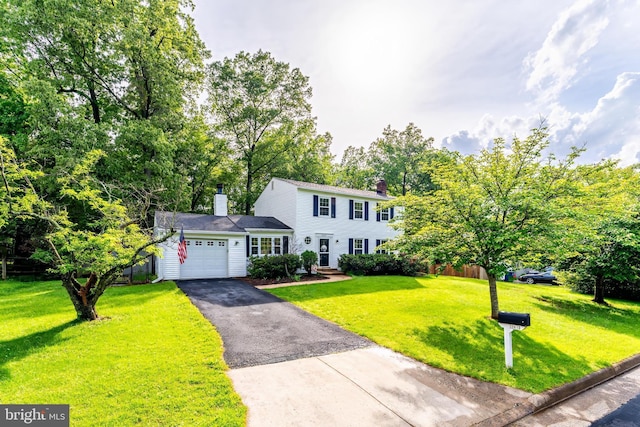 colonial house featuring a garage, a front lawn, a chimney, and driveway