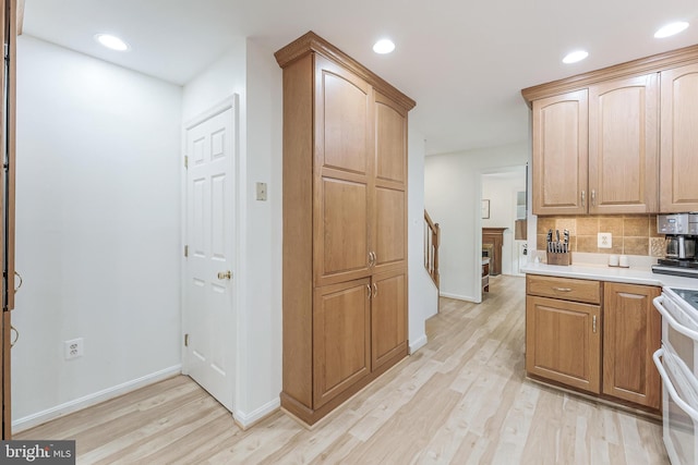 kitchen featuring light wood finished floors, white range, baseboards, and backsplash