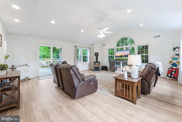 living room featuring light wood-style flooring, a ceiling fan, lofted ceiling with beams, visible vents, and a wood stove