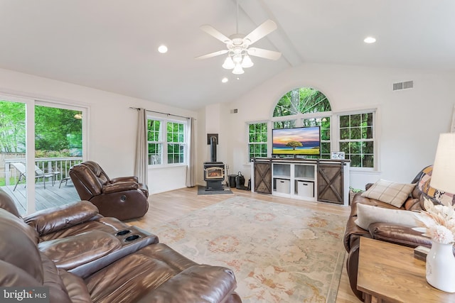 living area with wood finished floors, a ceiling fan, vaulted ceiling with beams, visible vents, and a wood stove