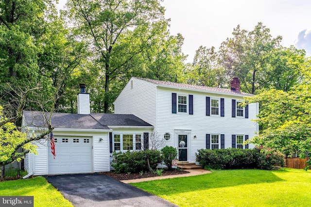 colonial inspired home with aphalt driveway, fence, a garage, a front yard, and a chimney