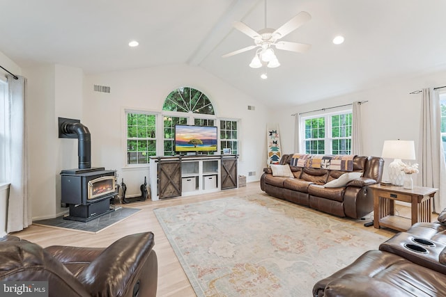 living area with a ceiling fan, visible vents, wood finished floors, lofted ceiling with beams, and a wood stove