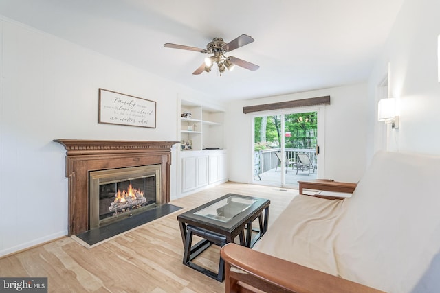 living area featuring built in shelves, a ceiling fan, a glass covered fireplace, and wood finished floors