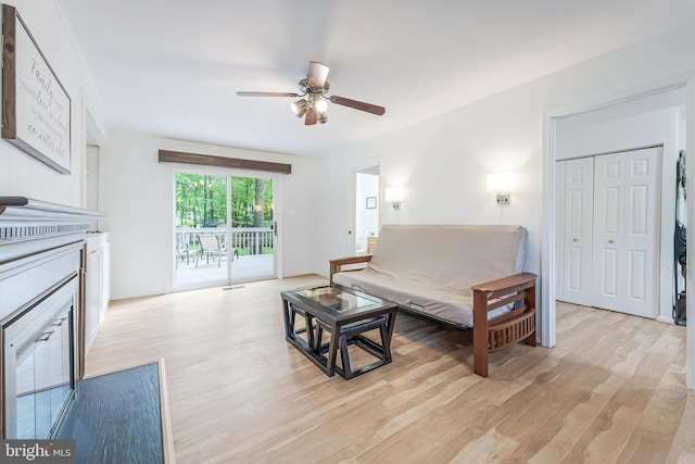 living area featuring light wood finished floors, a fireplace, and ceiling fan