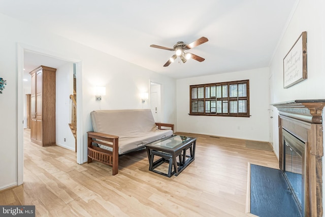 living area with baseboards, light wood-style flooring, a ceiling fan, and a fireplace with flush hearth
