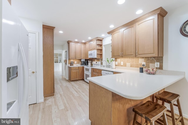 kitchen featuring light wood-style flooring, a breakfast bar, white appliances, a peninsula, and open shelves