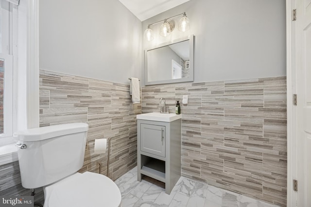 bathroom with tile walls, toilet, a wainscoted wall, and vanity