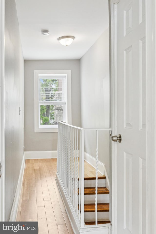 corridor with baseboards, an upstairs landing, and light wood-type flooring