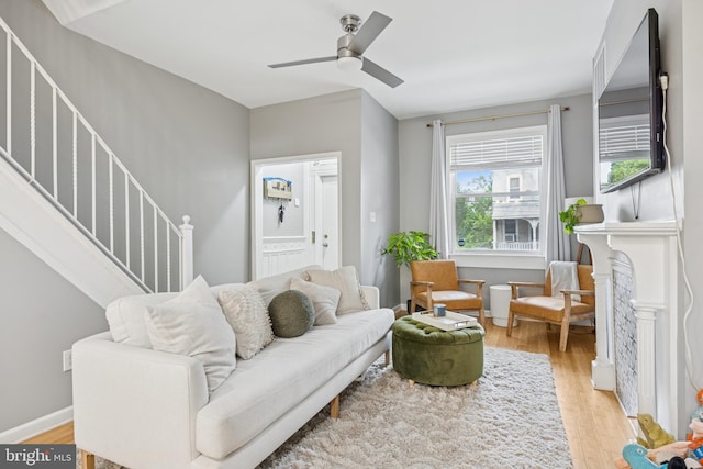 living area featuring a ceiling fan, stairs, a fireplace, and light wood-style flooring