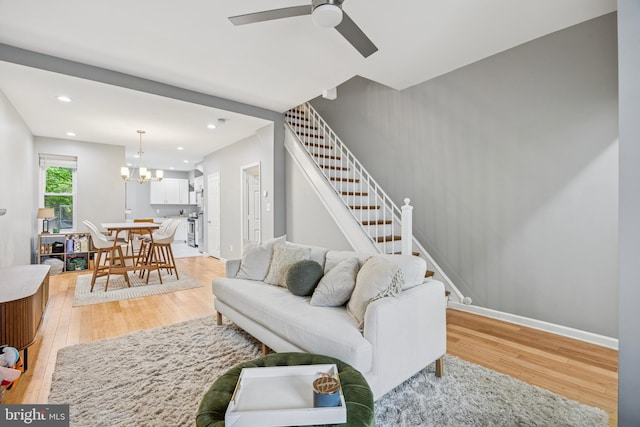 living room featuring stairway, recessed lighting, ceiling fan with notable chandelier, and light wood-style floors
