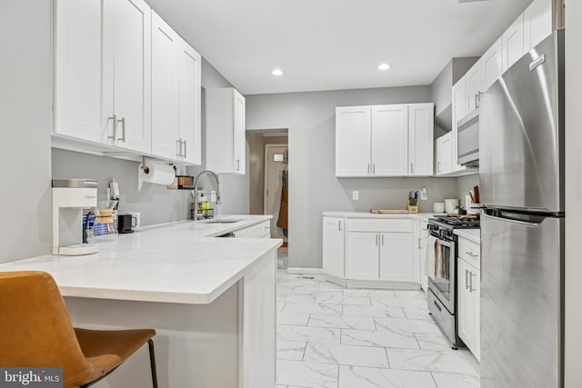 kitchen with a sink, a peninsula, stainless steel appliances, marble finish floor, and white cabinetry