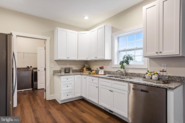 kitchen with stainless steel appliances, a sink, washer and dryer, dark wood finished floors, and white cabinetry