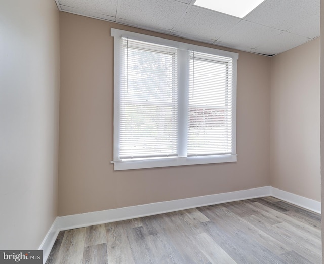 empty room featuring a drop ceiling, wood finished floors, and a healthy amount of sunlight