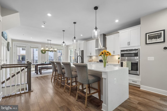 1653 Bandit Loop, Reston, VA 20190 - kitchen featuring wall chimney exhaust hood, stainless steel appliances, an island with sink, decorative backsplash, and white cabinetry