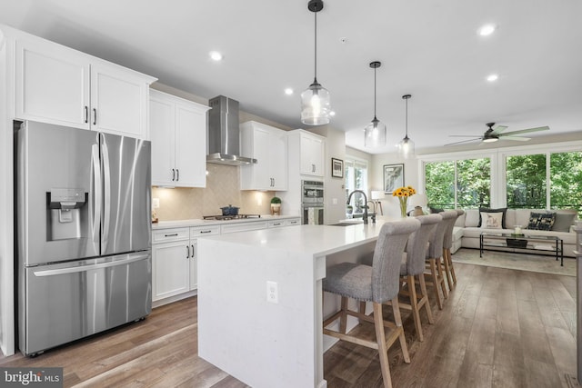 1653 Bandit Loop, Reston, VA 20190 - kitchen with appliances with stainless steel finishes, wall chimney range hood, a sink, white cabinets, and an island with sink