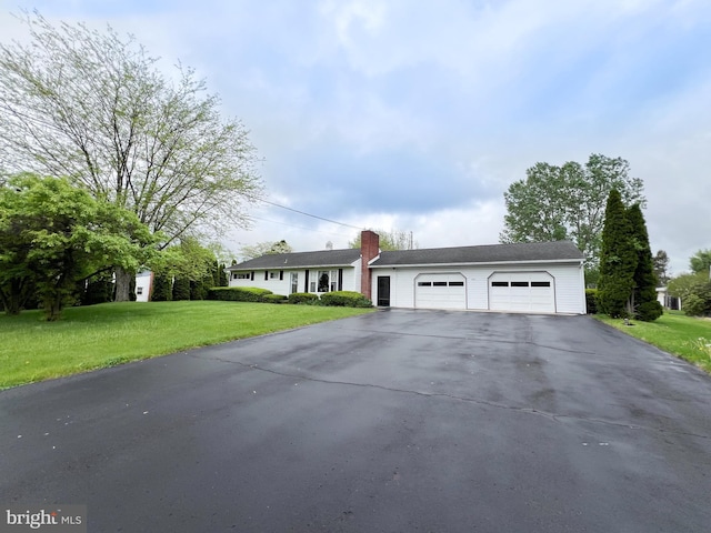 single story home featuring aphalt driveway, an attached garage, a chimney, and a front yard