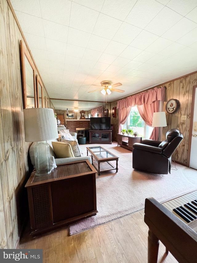 living area with wooden walls, wood finished floors, and a ceiling fan
