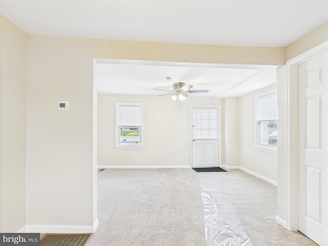 empty room featuring light colored carpet, a wealth of natural light, baseboards, and a ceiling fan