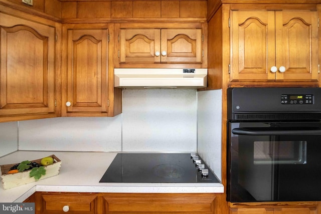 kitchen featuring black appliances, under cabinet range hood, light countertops, and brown cabinetry