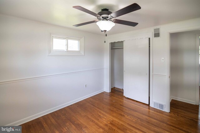 unfurnished bedroom featuring a closet, wood finished floors, baseboards, crown molding, and a ceiling fan