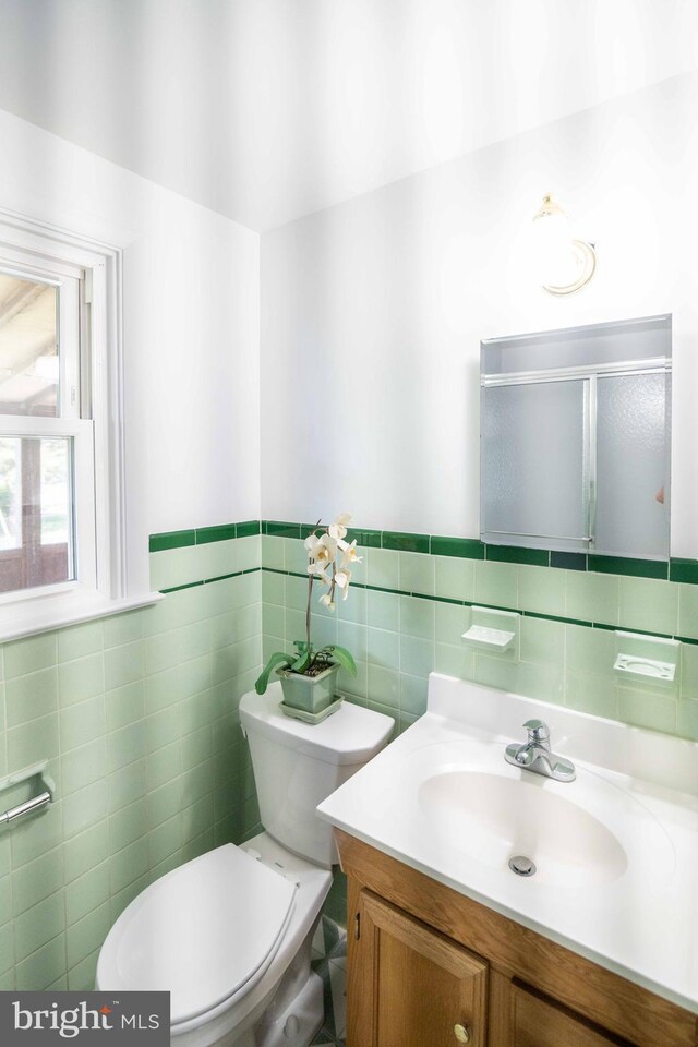 bathroom featuring tile walls, vanity, toilet, wainscoting, and an enclosed shower