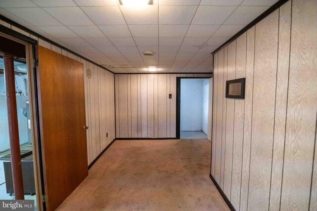 hallway featuring light carpet, wooden walls, and baseboards
