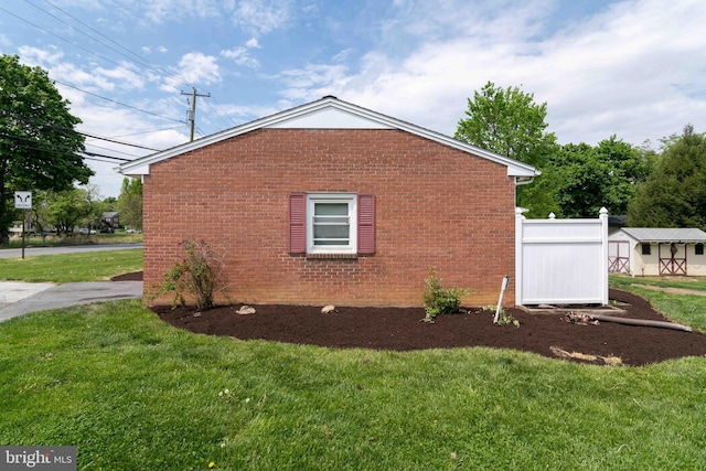 view of property exterior with a storage unit, a lawn, an outbuilding, and brick siding