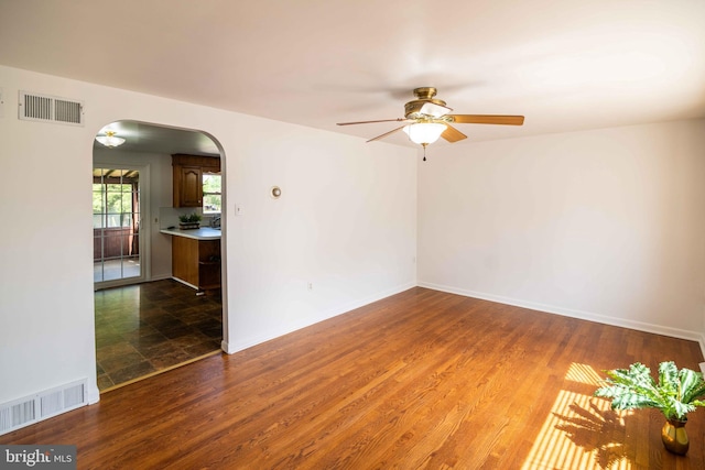 unfurnished room featuring arched walkways, ceiling fan, wood finished floors, and baseboards