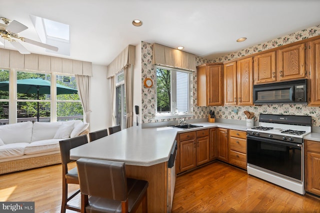kitchen featuring white range with gas stovetop, black microwave, a skylight, light countertops, and a breakfast bar area