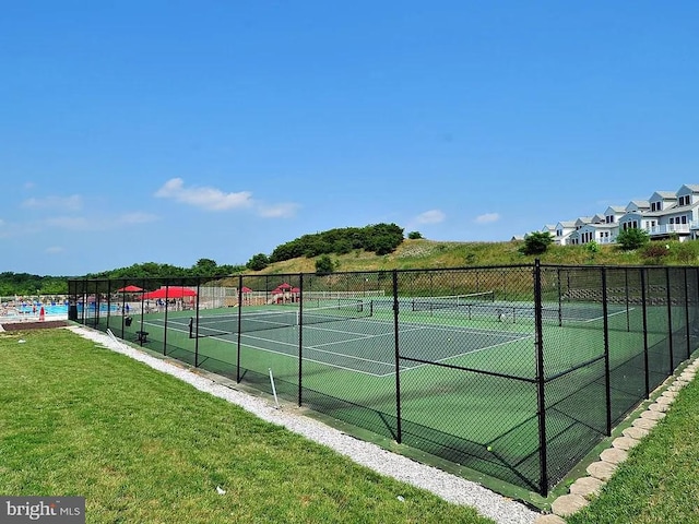 view of tennis court with a yard and fence