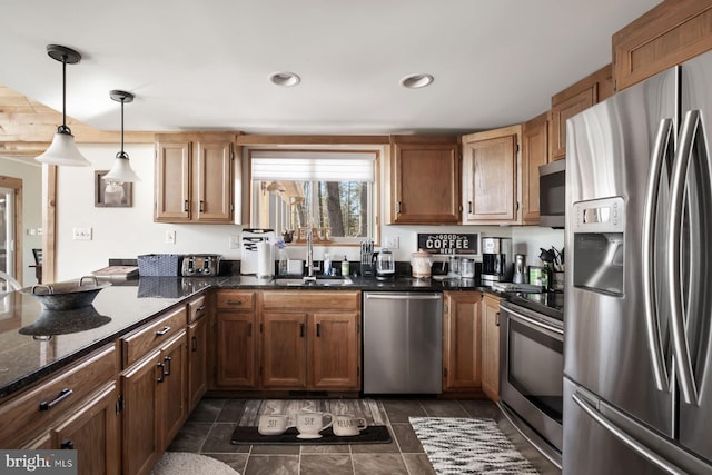 kitchen featuring stainless steel appliances, a sink, pendant lighting, a peninsula, and dark stone counters