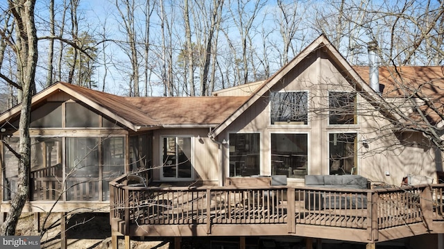 rear view of house featuring a deck, a sunroom, and a shingled roof