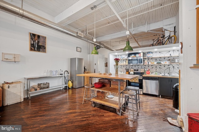 interior space featuring beam ceiling, appliances with stainless steel finishes, a high ceiling, and wood finished floors