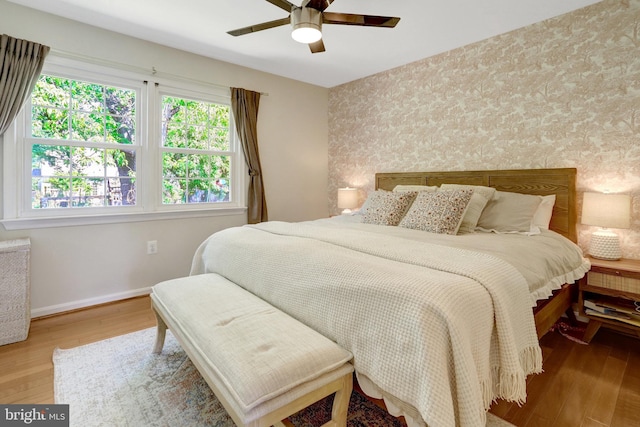 bedroom with baseboards, a ceiling fan, an accent wall, and wood finished floors