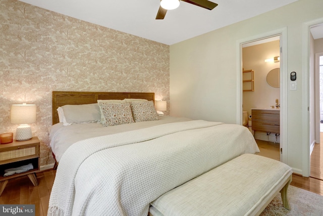 bedroom with a ceiling fan, wallpapered walls, baseboards, ensuite bathroom, and wood finished floors