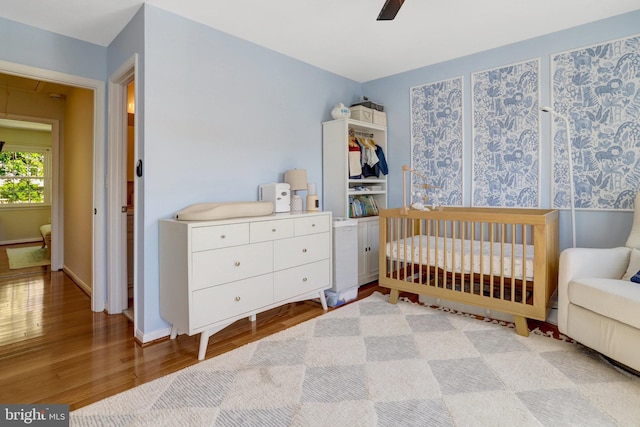 bedroom with a nursery area, a ceiling fan, wood finished floors, and baseboards